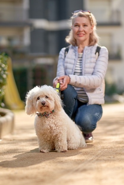 Attractive middle-aged blond woman walking with dog in summer city.