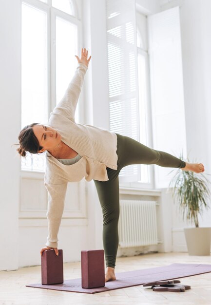 Attractive middle aged brunette woman in sportswear ptactice yoga with equipment in the light studio