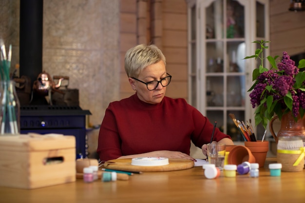 Attractive middle-aged woman draws in cozy country house with fireplace