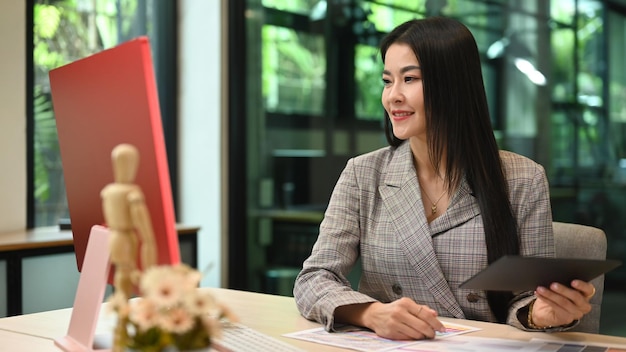 Attractive millennial businesswoman hand holding digital tablet and reading information on computer display