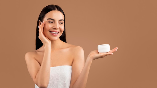 Attractive millennial halfnaked brunette woman applying face cream