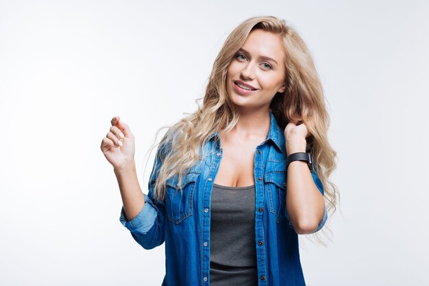 Attractive model. Gorgeous fair-haired young woman posing on grey background and holding her one hand in hair