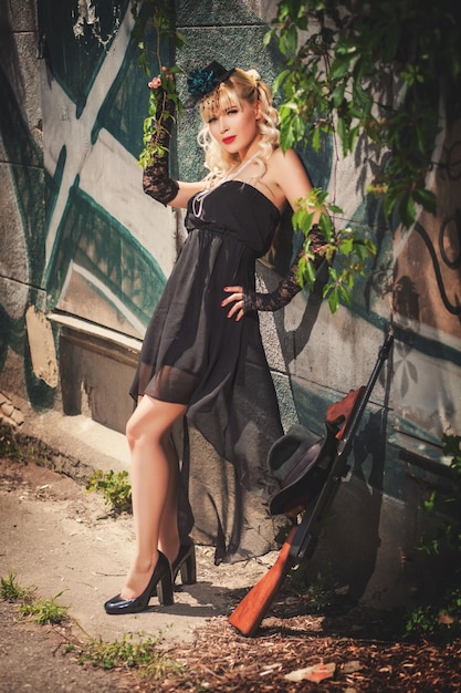 Attractive model standing in front of stone wall with graffiti near gun