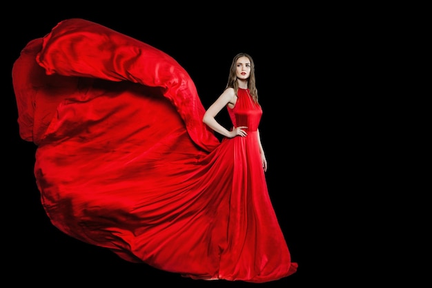 Attractive model woman in red silky evening gown standing isolated on black background