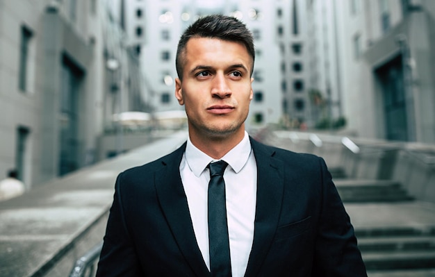 Attractive modern businessman in a black suit stands with a serious look in front of him against the backdrop of the city