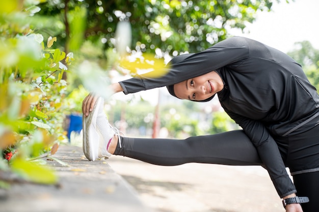 Attraente donna asiatica musulmana strecth la gamba durante il tempo di sport all'aperto in una giornata di sole