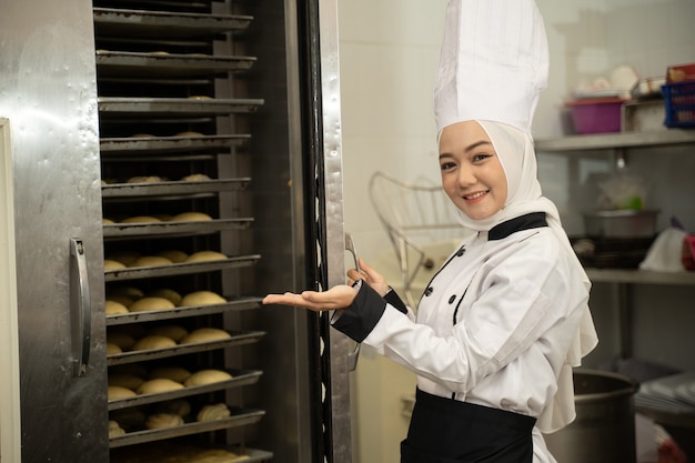 Attractive muslim woman Baker smiling at the camera in the kitchen of the bakery with big oven