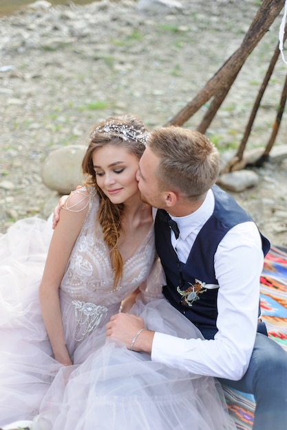 An attractive newlywed couple, a happy and joyful moment. Man and woman hug and kiss in holiday clothes. Wedding Cermonia with Boho-style dÃÂ©cor by the river in the fresh air.