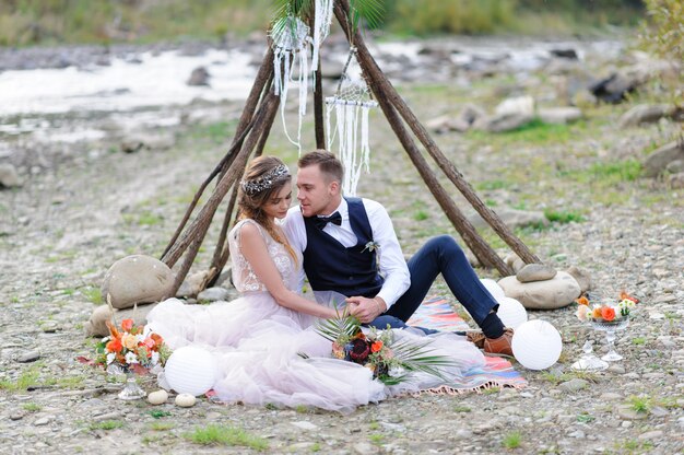 An attractive newlywed couple, a happy and joyful moment. Man and woman hug and kiss in holiday clothes. Wedding Cermonia with Boho-style dÃÂ©cor by the river in the fresh air.