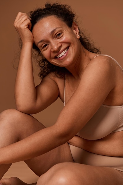 Attractive nude African American woman in underwear smiles toothy smile looking at camera. Body positivity, self-acceptance and confidence, body love concept with copy ad space