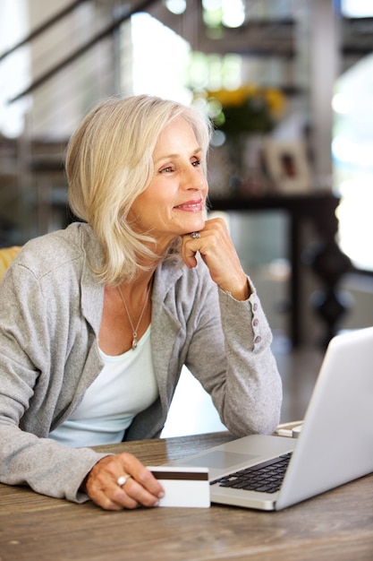 Donna più anziana attraente con il computer portatile e la carta di credito