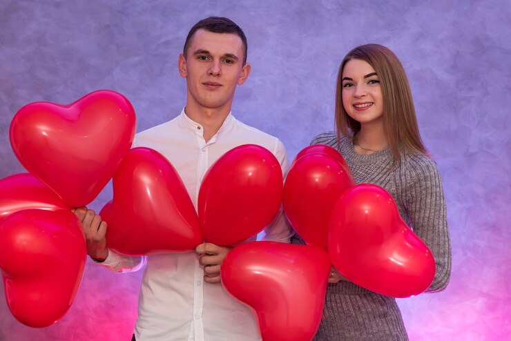 Фотография привлекательная пара с красными воздушными шарами, улыбаясь в студии. влюбленная пара