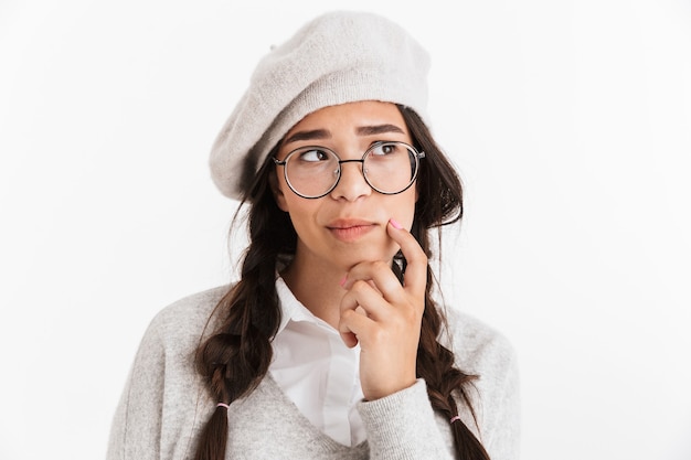 Attractive pensive schoolgirl wearing unifrom standing isolated over white wall