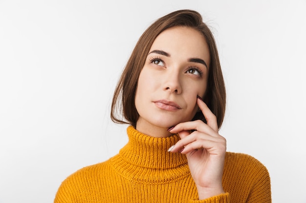 Attractive pensive young woman standing isolated over white wall