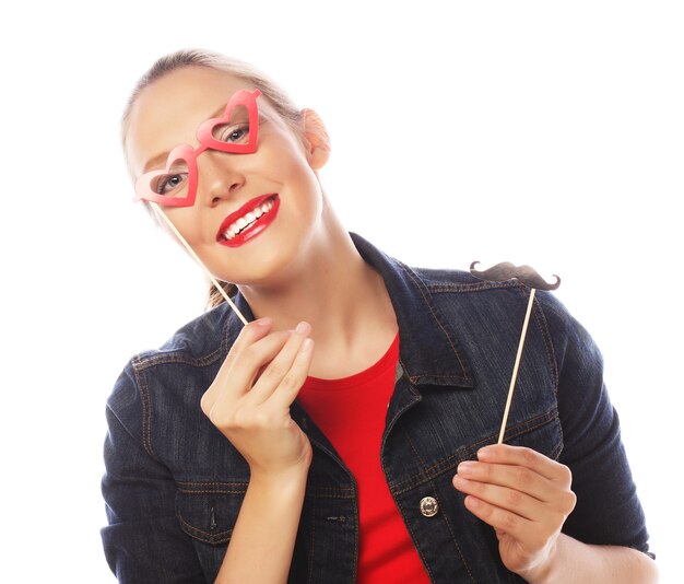 Attractive playful young woman holding mustache and glasses on a stick. Ready for party.