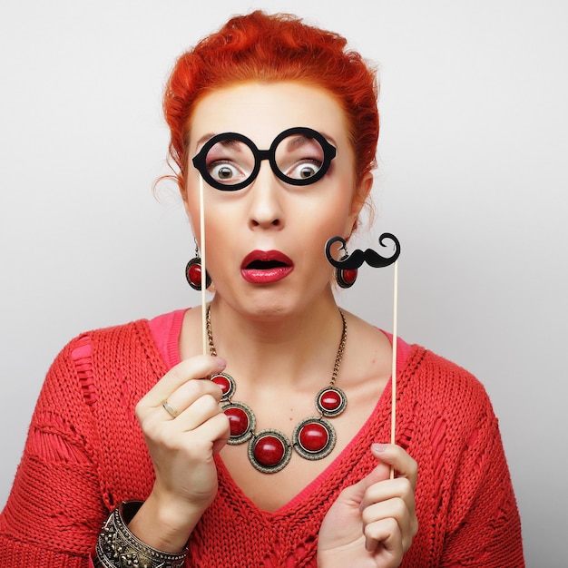 Attractive playful young woman holding mustache and glasses on a stick Ready for party