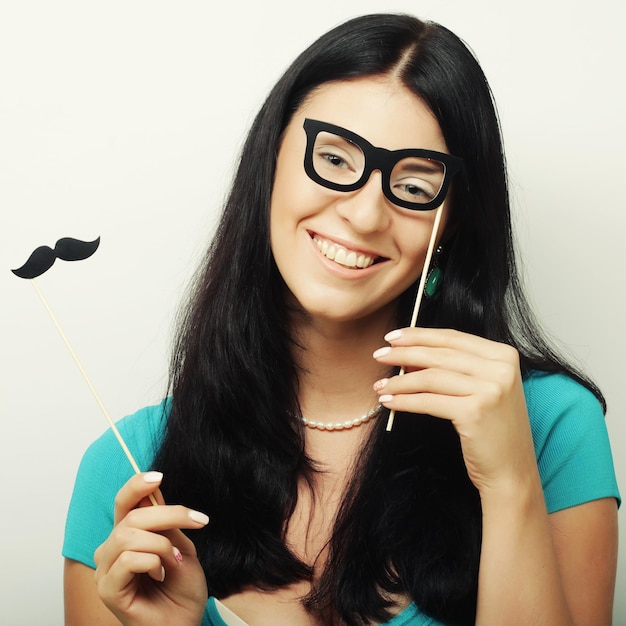 Attractive playful young woman holding mustache and glasses on a