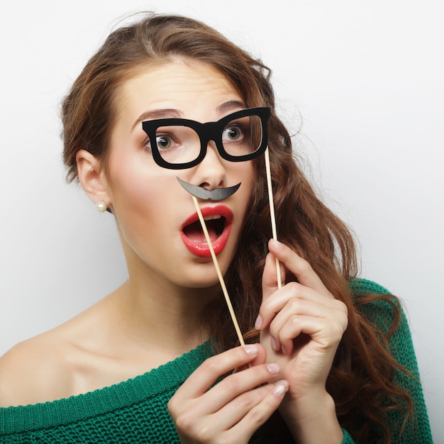 Attractive playful young woman holding mustache and glasses