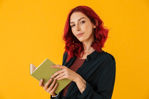 attractive pleased woman with curly red hair holding exercise book isolated