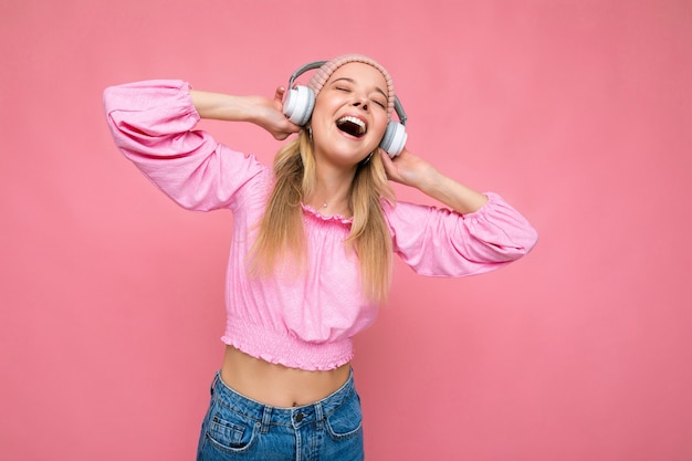 Attractive positive emotional smiling young blonde woman wearing pink blouse and pink hat isolated