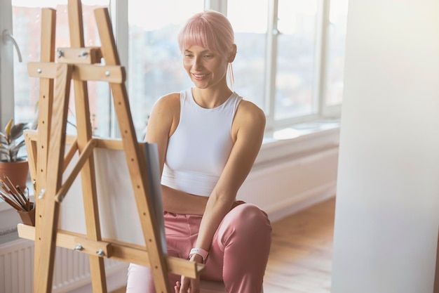 Attractive positive lady artist at work upon new picture at home