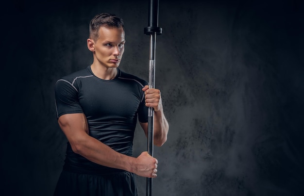 Attractive power lifter holds barbell over dark grey background.