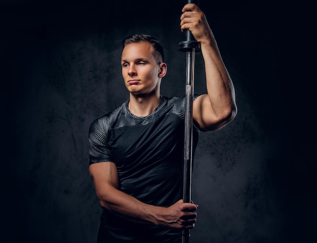 Attractive power lifter holds barbell over dark grey background.