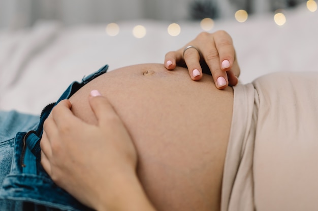 Attractive pregnant woman is sitting in bed and holding her belly.