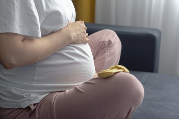 Attractive pregnant woman is sitting on the couch and holding her belly Last months of pregnancy