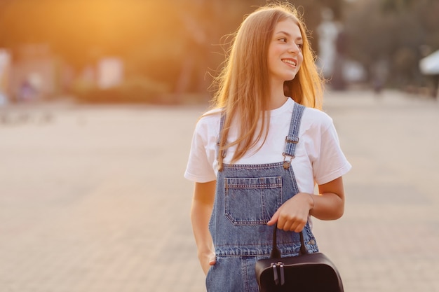 Attractive pretty girl with briefcase walk on street at morning sunrise lights