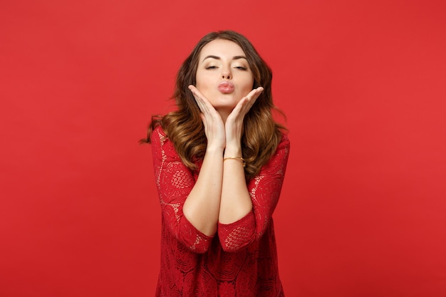 Attractive pretty young woman in lace dress blowing sending air kiss, putting hands on head isolated on bright red background in studio. People sincere emotions, lifestyle concept. Mock up copy space.