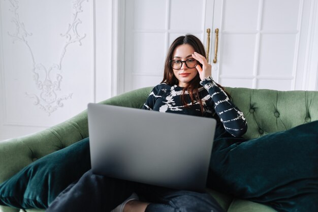 Attractive pretty young woman using computer, sitting on comfortable sofa