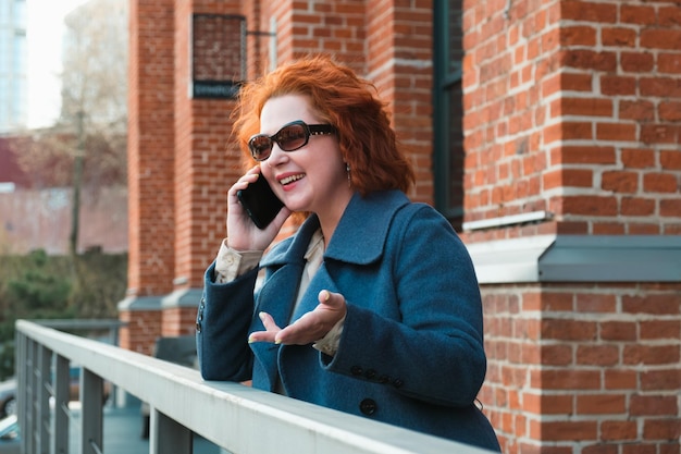 Attractive redhaired woman in a blue coat is talking on a mobile phone