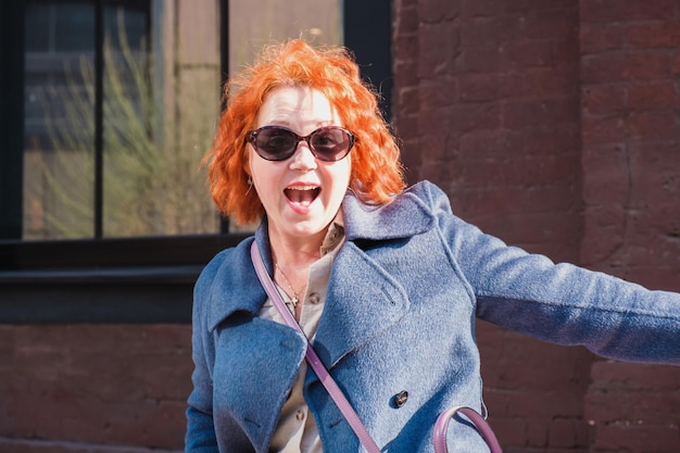 Привлекательная рыжеволосая женщина в солнечных очках смеется с открытым ртом