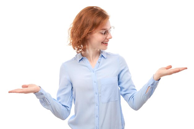 Attractive redhead girl promoter in blue business shirt holding something in hand demonstrating empty space with excited face isolated on white background