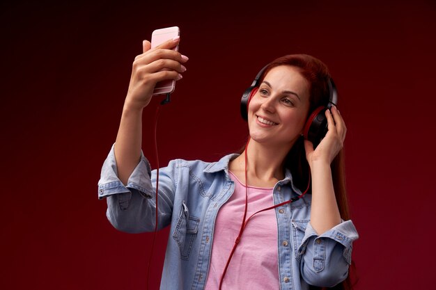 Gioia attraente della donna di redhead, cuffie positive e da portare, tenenti smartphone