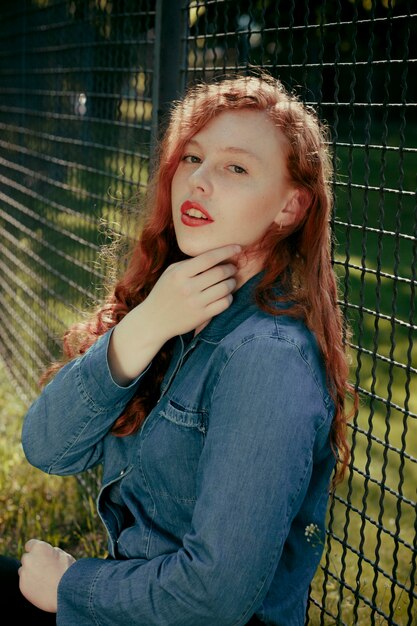 Attractive redhead young model sitting near fence  in rays of sun