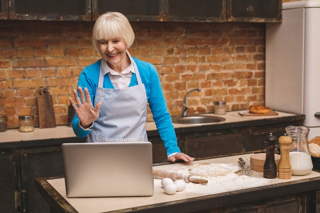 매력적인 수석 세 여자는 부엌에서 요리입니다. 맛있는 제빵을 만드는 할머니. 노트북을 사용합니다.
