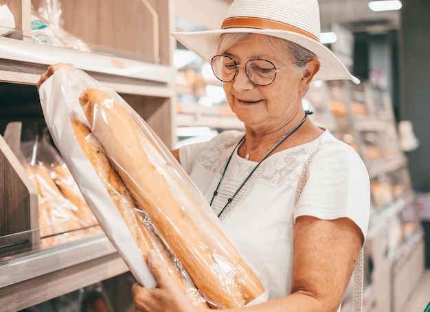 Attractive senior customer woman with hat buys bread for family in supermarket