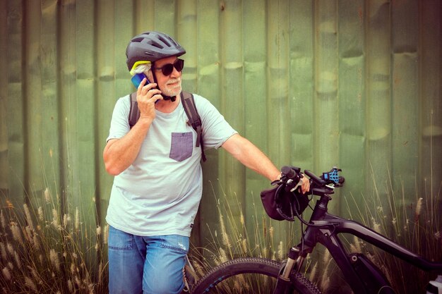Attractive senior man with helmet and backpack using mobile\
phone while enjoying sport activity with electric bicycle in\
outdoors sustainable mobility concept