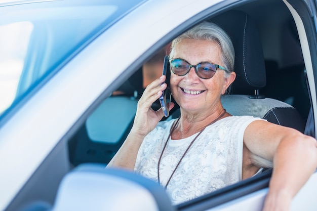 車で駐車し、スマートフォンを使って話したり笑ったりする魅力的な年配の女性-アクティブな高齢者