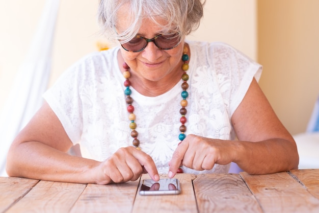 Attractive senior woman sitting and messaging with telephone and smiling Grey hair and sunglasses