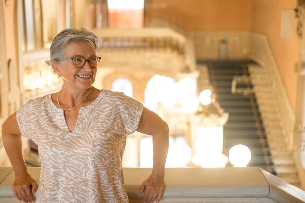 Attractive senior woman visiting an old historic palace in Barcelona, standing on the stairs smiling