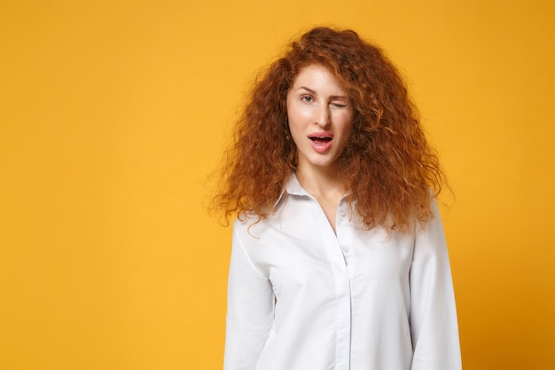 Attraente ragazza sexy giovane donna dai capelli rossi in camicia bianca casual in posa isolata sul muro giallo arancione