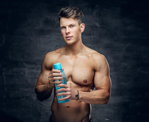 The attractive shirtless muscular guy holds a bottle of water.