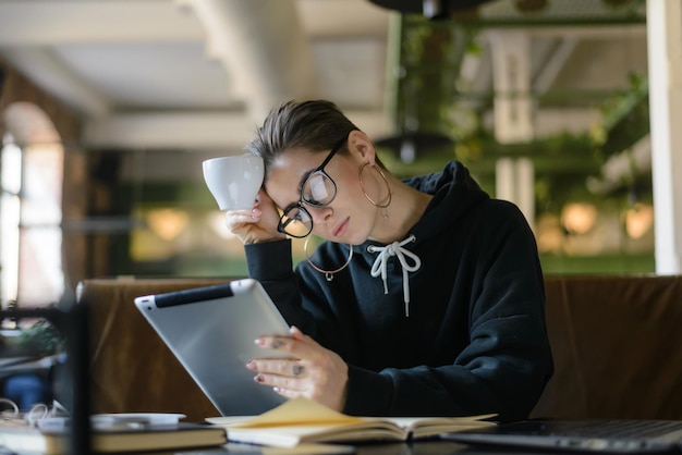 Attractive shorthair hipster girl in trendy spectacles studying with modern tablet with internet connection