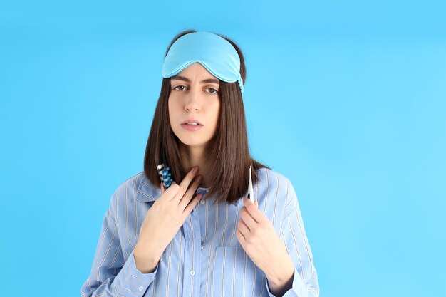 Attractive sick woman in sleep mask on blue background