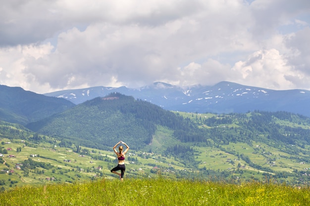 La giovane donna esile attraente che fa l'yoga si esercita all'aperto