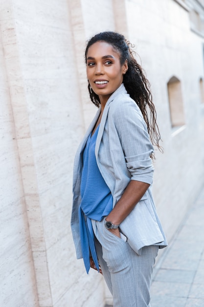 Attractive smiling african business woman standing outdoors at the city