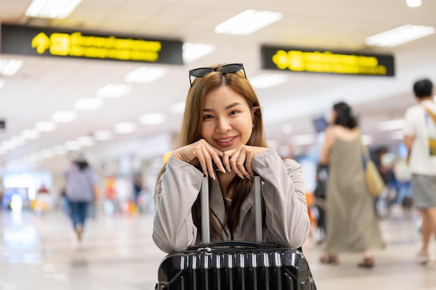 an attractive smiling asian female traveler with her luggage is in the airport
